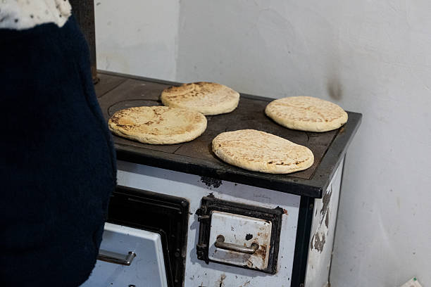 Four round flatbreads are cooking directly on the surface of an old-fashioned wood-burning stove. The rustic setting and slightly charred bread tops evoke a traditional, home-style baking method with nostalgic charm.