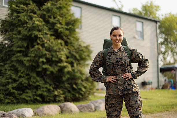 Woman Marine returning home in uniform with tactical backpack, standing outdoors and smiling confidently, proud and ready