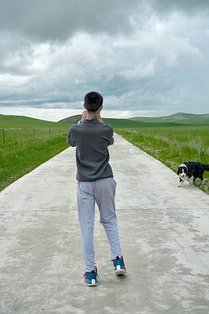 Boy walking on a long quiet road with his border collie dog in green countryside