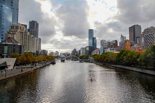 A view of Melbourne showing the Yarra River and surrounding modern high-rise buildings under a cloudy sky.