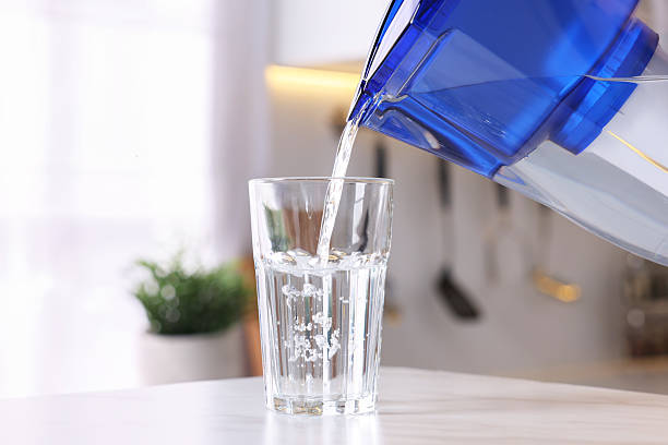 istock Pouring water from filter jug into glass in kitchen, closeup 2244076446