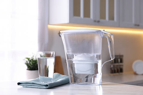 istock Water filter jug and glass on white marble table in kitchen, closeup 2244076459