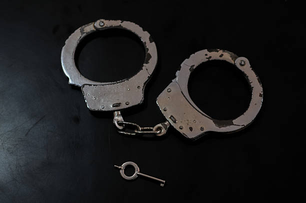 Close Up View of Metal Handcuffs with the Key Inserted on a Dark Reflective Surface