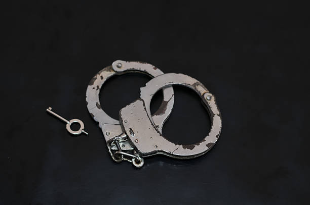 istock Close Up View of Metal Handcuffs with the Key Inserted on a Dark Reflective Surface 2244076715