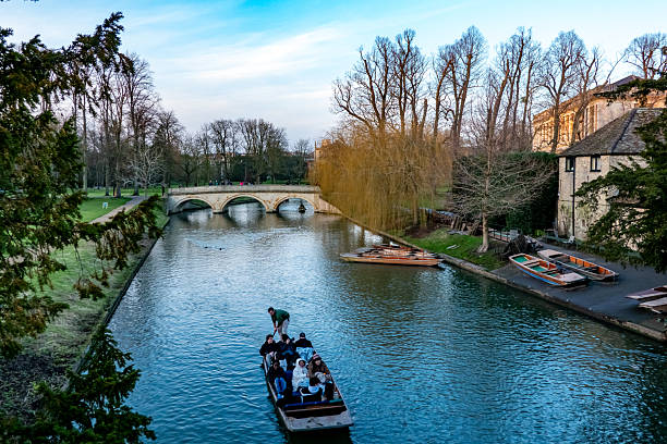 Cambridge, UK - February 02, 2025: A picturesque scene of a group of people being punted down the River Cam, passing under a stone bridge, near the Cambridge University buildings.