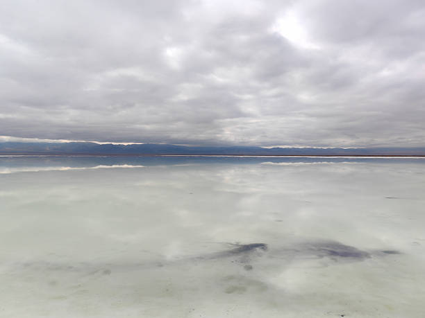 On a cloudy day, the salt lake's surface is as flat as a mirror, reflecting the clouds and distant mountains