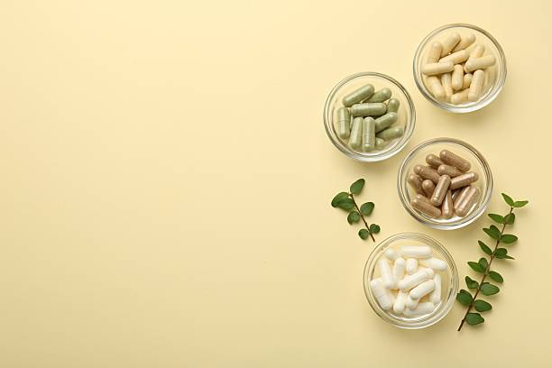 istock Different vitamin capsules in bowls and branches on pale yellow background, flat lay. Space for text 2244082828