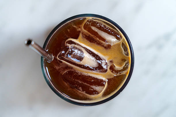 Top view of a glass of iced Americano coffee with a stainless steel straw on a marble table.