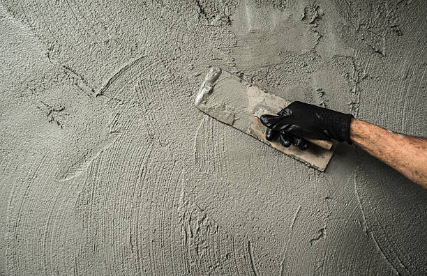 istock Hand worker plaster cement wall background with hand holding work trowel handle and mix wet fresh grey mortar concrete texture at construction house site well space for text presentation 2244092186