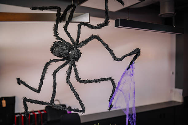 Large black spider decoration hanging from ceiling with purple web strands, creating a spooky atmosphere in a modern indoor space, perfect for Halloween-themed events and parties