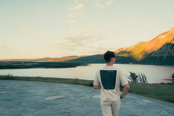 Man admiring a tranquil lake and mountain view, nature's beauty unfolds. Waterton, AB