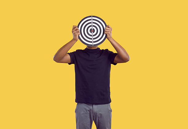 istock Unknown dark-skinned man hides his face behind darts board on yellow background. 2244099520