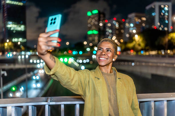 istock Woman smiling taking selfie in illuminated city at night 2244100404