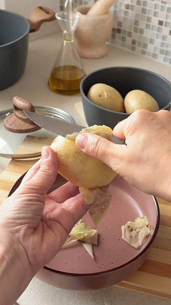 istock Anonymous peel boiled potatoes with knife in the kitchen. 2244102282