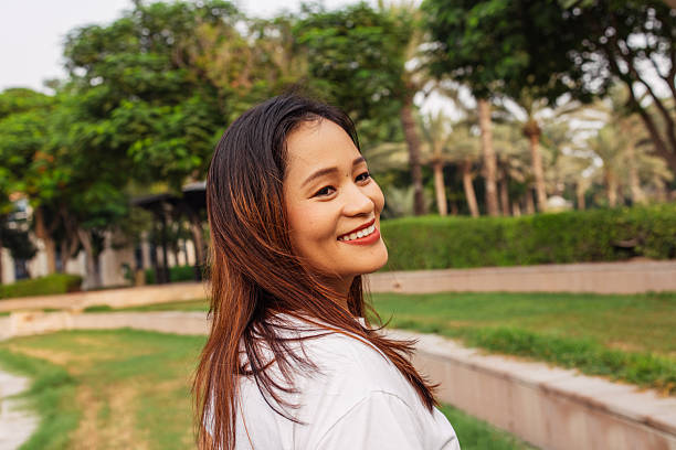 A joyful woman wearing a white shirt, enjoying a sunny day in a lush green park. The photo captures a carefree moment, emphasizing happiness and outdoor enjoyment. The vibrant greenery and natural surroundings enhance the lively and positive atmosphere, making it an inspiring portrayal of leisure and positivity.