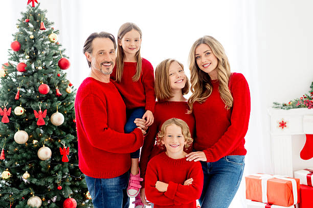 A warm festive family gathers in red sweaters by a decorated Christmas tree in a bright living room, sharing joy and togetherness during the holiday season.