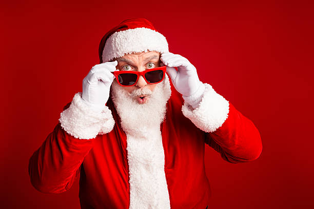 istock Funny Santa in red suit with white beard and sunglass strikes a playful pose against a red background for Christmas stock photo 2244104708