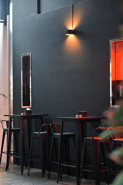 istock Dark gray wall with warm wall sconce above black high tables and bar stools interior 2244107431