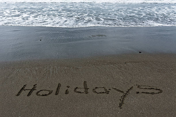 Waves lapping towards the word Holidays written in the sand.