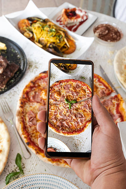 istock Hand holding smartphone photographing pizza on restaurant table 2244115719