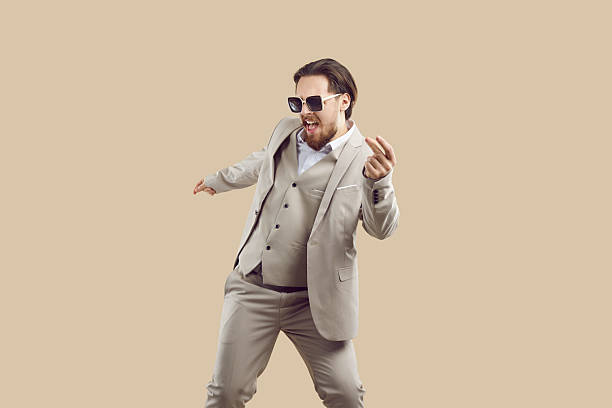 istock Cheerful cool man in three-piece suit rejoices and has fun dancing on beige background. 2244122050
