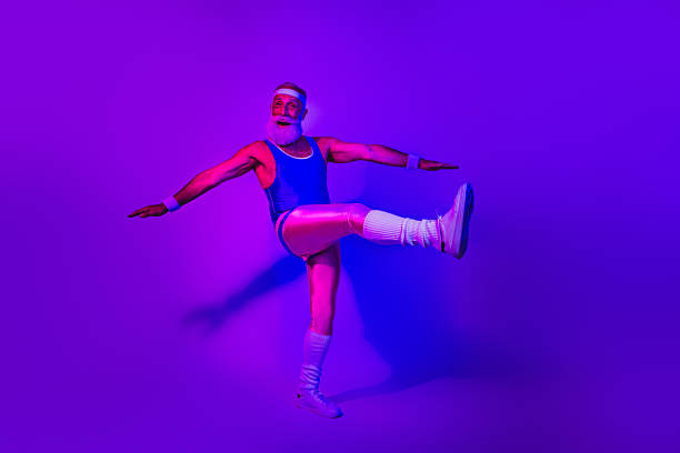 istock Energetic bearded senior athlete in a retro jumpsuit performing a dynamic kick under purple blue neon lights 2244124065