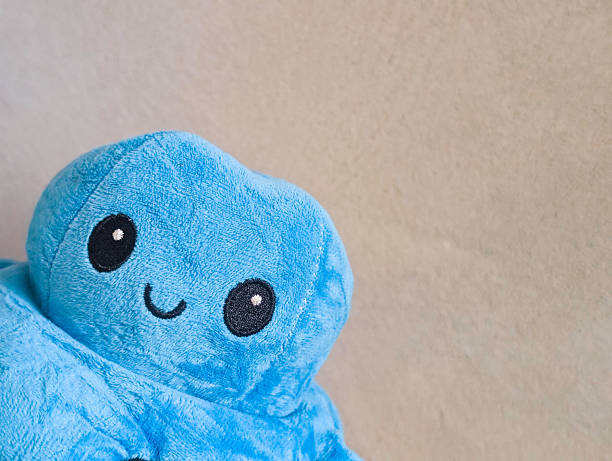 a close-up, cropped shot of a happy blue reversible octopus plush toy, smiling against a neutral light-colored background. this adorable stuffed animal represents positive mood, emotional well-being, and playfulness. ideal for designs related to children's toys, emotional regulation, psychology, mental health, and cheerful concepts with copy space for text.
