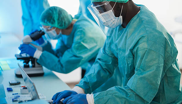 istock Medical workers in hazmat suit working with microscope inside laboratory hospital wearing safety masks - Healthcare, longevity and medical research concept - Focus on african man face 2244132750