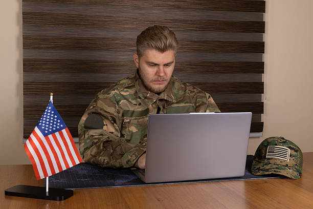 istock Man in military uniform using laptop in desert outpost 2244133480