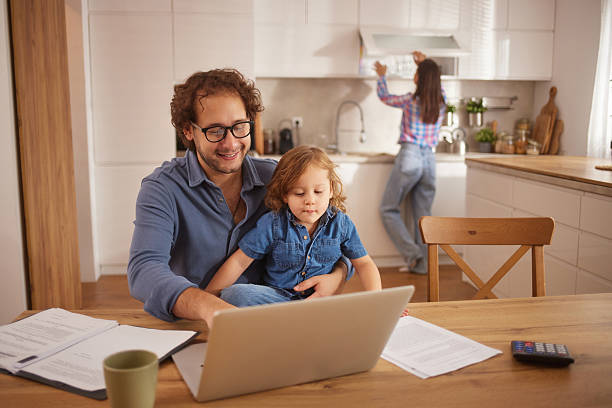 istock Father working on laptop with son on his lap in kitchen 2244136346