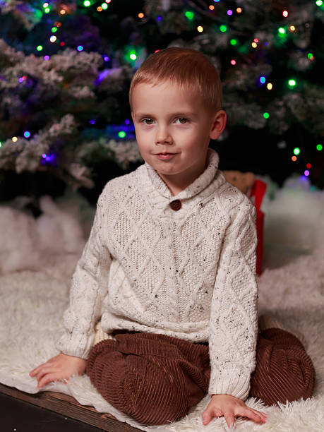 istock Boy sitting near Christmas tree in cozy sweater 2244136631