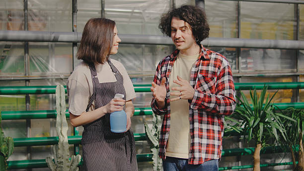 istock Two individuals engage in a conversation while holding a cleaning bottle in a greenhouse filled with plants on a sunny day 2244137250
