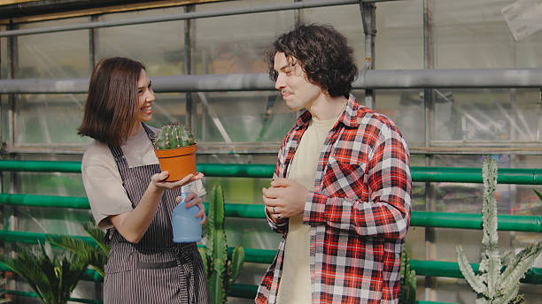 istock Two people at a plant shop smiling and talking while showcasing a small potted cactus in a flower greenhouse filled with greenery 2244137574