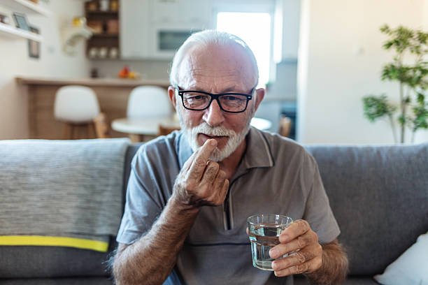 istock Smiling senior man sitting at a table in his home, taking daily medication from a blister pack while having a glass of water nearby, embracing a routine of health and wellness. 2244141027