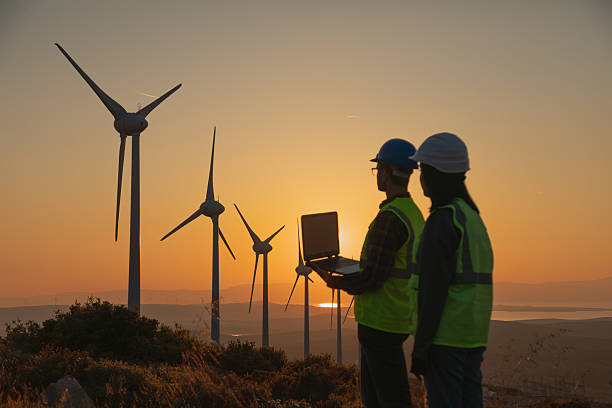 istock Engineers with Safety Helmets and Laptop at Wind Farm During Sunset, Focus on Renewable Energy, Sustainability, and Green Technology 2244142321