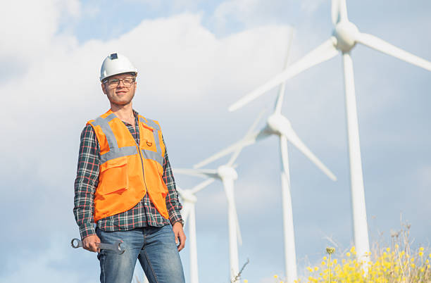 Renewable energy engineer looking at the sky with a wind power generator in the background. Maintenance operator with individual protection equipment in a wind farm. Leadership concept.