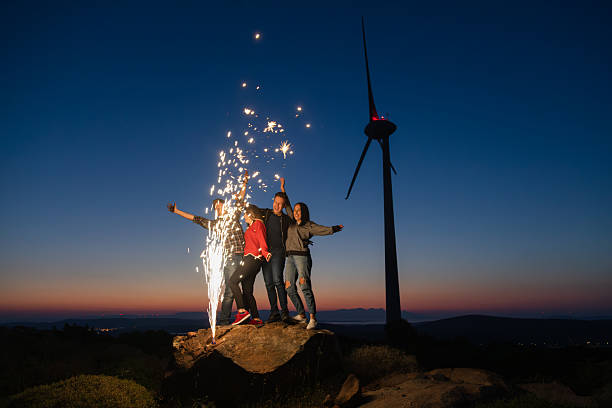 Silhouette shot group of cool teen hipster friends dancing and celebrating with sparklers during partying and enjoy natural wind farm area at blue hour time outdoor. XXXL size
