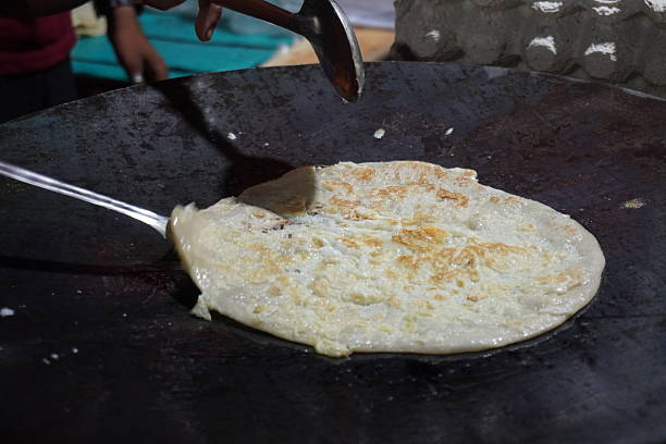 Street food vendor cooking Indian flatbread or egg paratha on large iron tawa