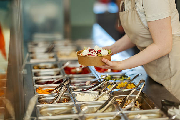 Worker holding a takeaway bowl filled with a healthy, fresh salad at a self-service restaurant buffet