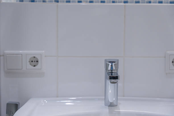 Bathroom sink faucet. A close-up of a modern chrome faucet on a white sink with tiled wall background. Clean and minimalist bathroom interior.