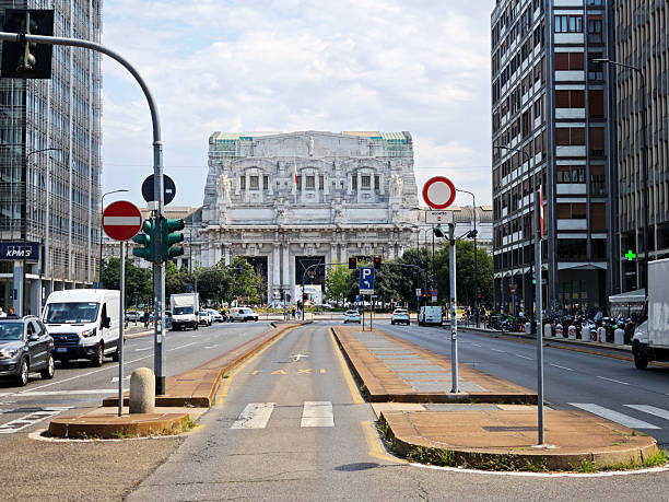 Traffic on the street at historical Milano Centrale railway station, Milan main railway station. People walking on the sidewalk.