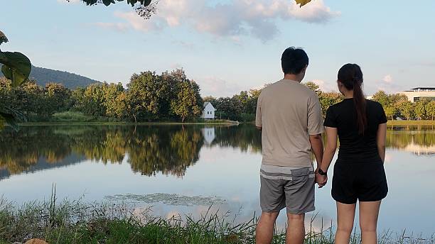 A couple is standing by a lake, holding hands and enjoying the view