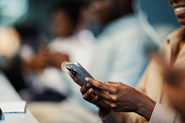Woman's hands holding and using a mobile phone, texting or browsing social media, with people in the background