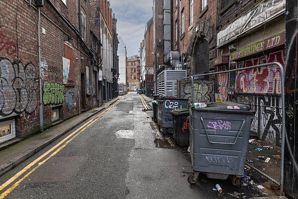 Manchester, uk, January 19th 2025 Graffiti-Laden City Alley With Trash Bins, Brick Walls, and Wet Street Scene