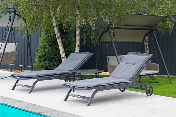 istock Two modern lounge chairs with gray cushions on a tiled patio by the pool 2244177057