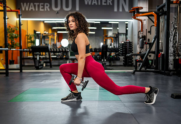 istock Woman exercising with dumbbell doing lunge at gym 2244177578