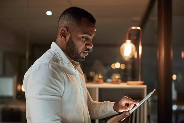 istock Focused Man in White Shirt Using Tablet in Modern Office at Night 2244179512