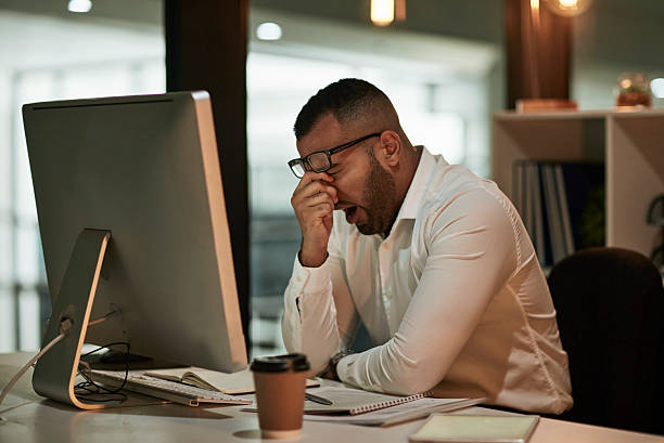 istock Stressed Office Worker Rubbing Eyes at Computer Desk in an Open Office Environment 2244180075