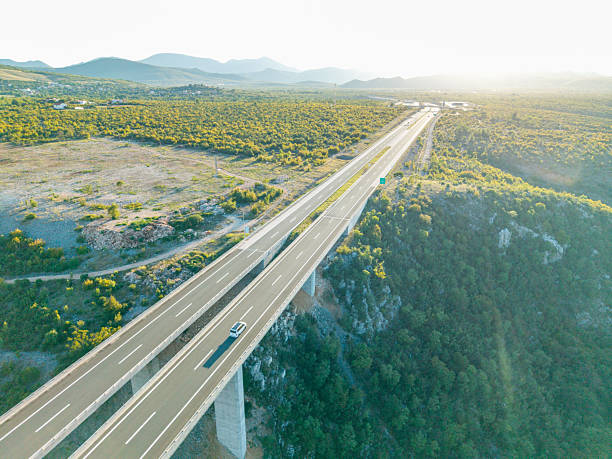 Aerial view of a long elevated highway bridge crossing a lush green valley with hills in the background. Scenic landscape with road infrastructure and natural vegetation. Mountain valley with bridge.
