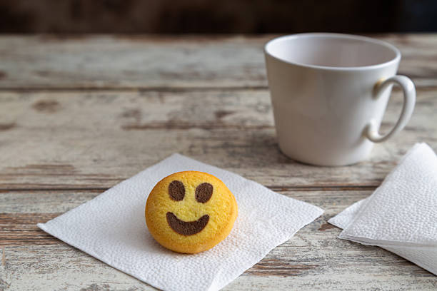 istock Shortbread cookie shaped like a smiley emoji lying on a white napkin on a wooden table next to a white cup, close-up, selective focus. 2244187389